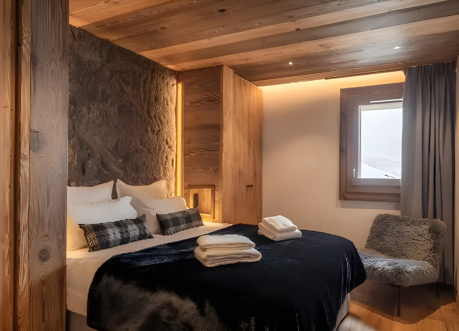 Chambre avec lit double, tête de lit en pierre apparente et habillage en bois