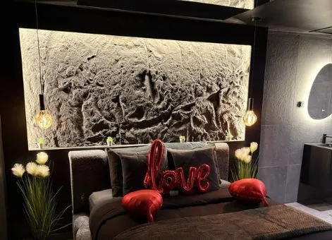 Chambre à literie noire et au mur derrière le lit en roche noire.