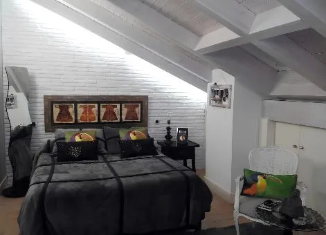 Chambre mansardée avec lit double, tête de lit en briques blanches et poutres apparentes